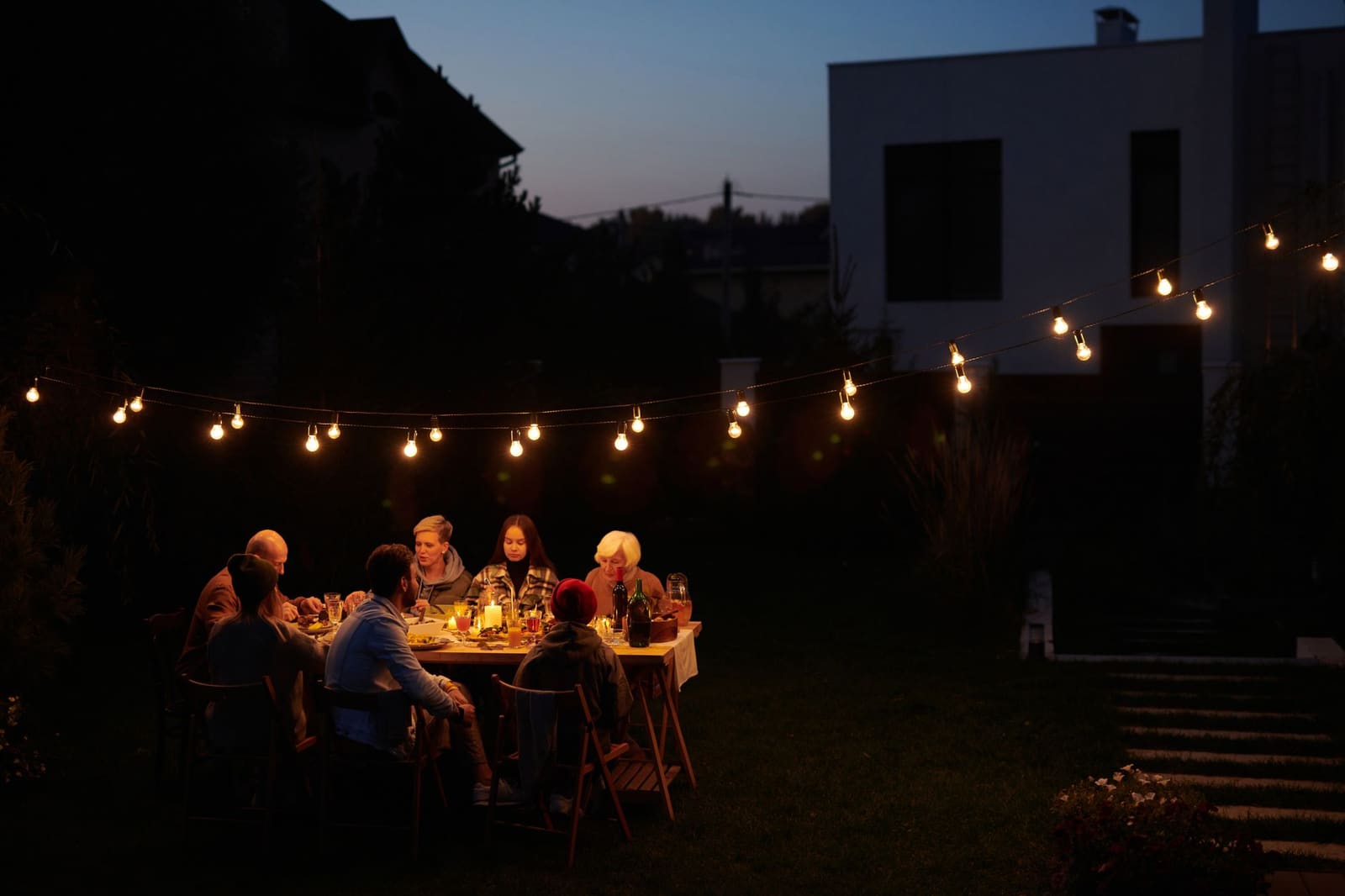 Repas en famille dans un jardin éclairé par des guirlandes lumineuses